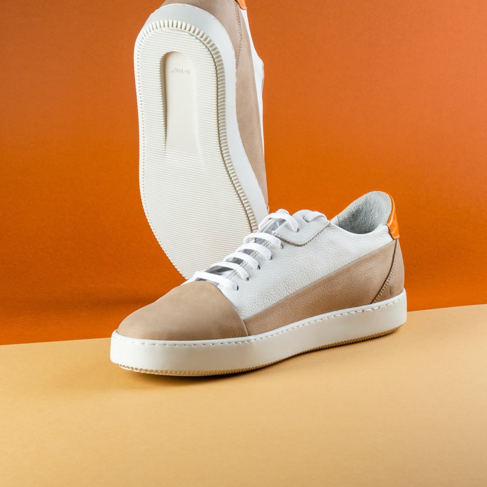 1. A single beige and white sneaker with its sole facing upwards, set against a dual-tone background with orange at the top and yellow at the bottom.